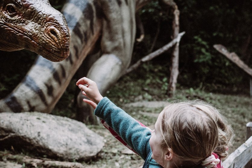 Ein Mädchen streckt seine Hand nach dem Kopf eines Dinosauriers aus.